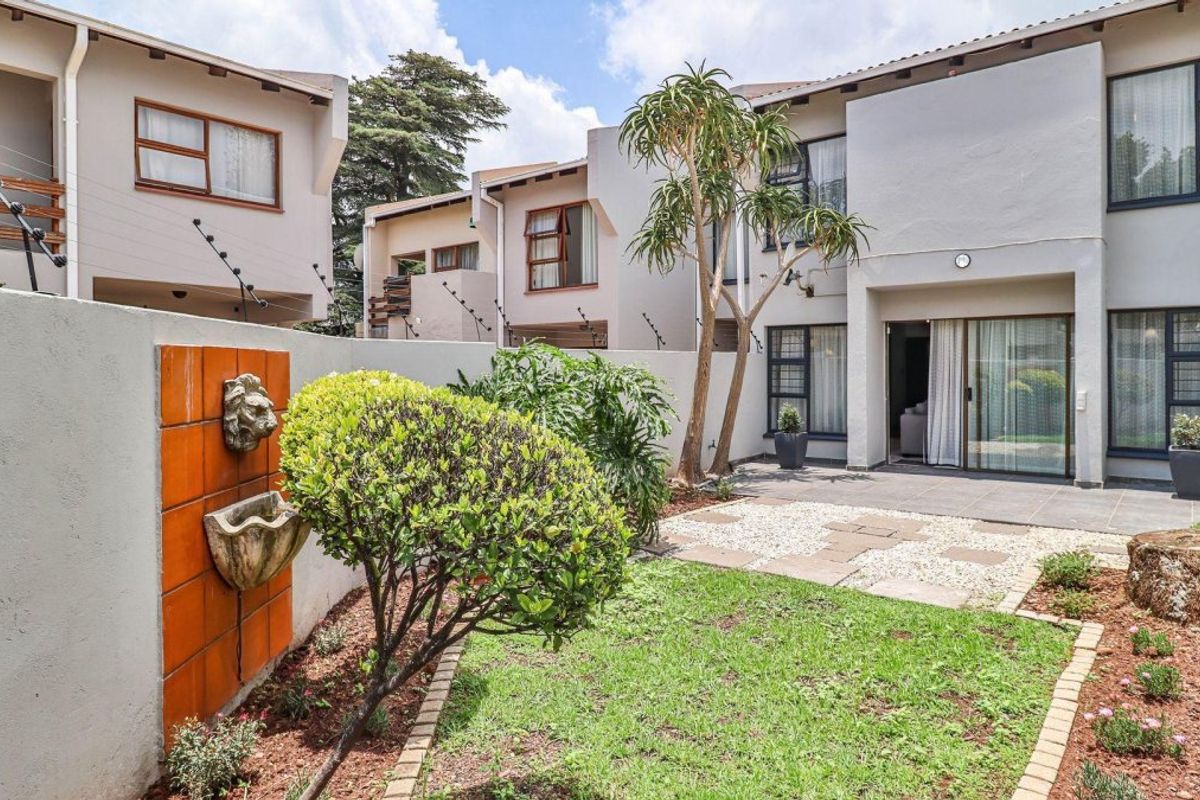 A well-maintained rear courtyard featuring a paved patio, landscaped garden, and a decorative wall-mounted water feature, providing a private outdoor living space.
