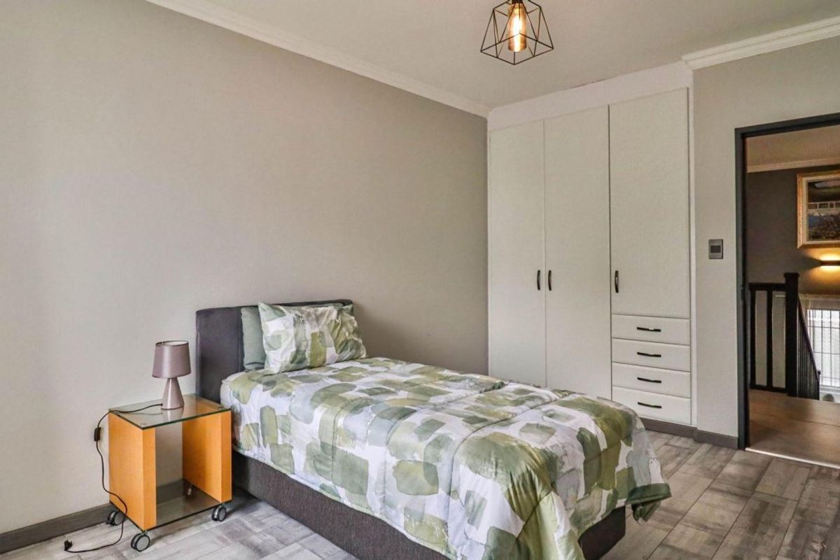 A well-maintained bedroom featuring built-in cupboards, modern laminate flooring, and a contemporary pendant light fixture.