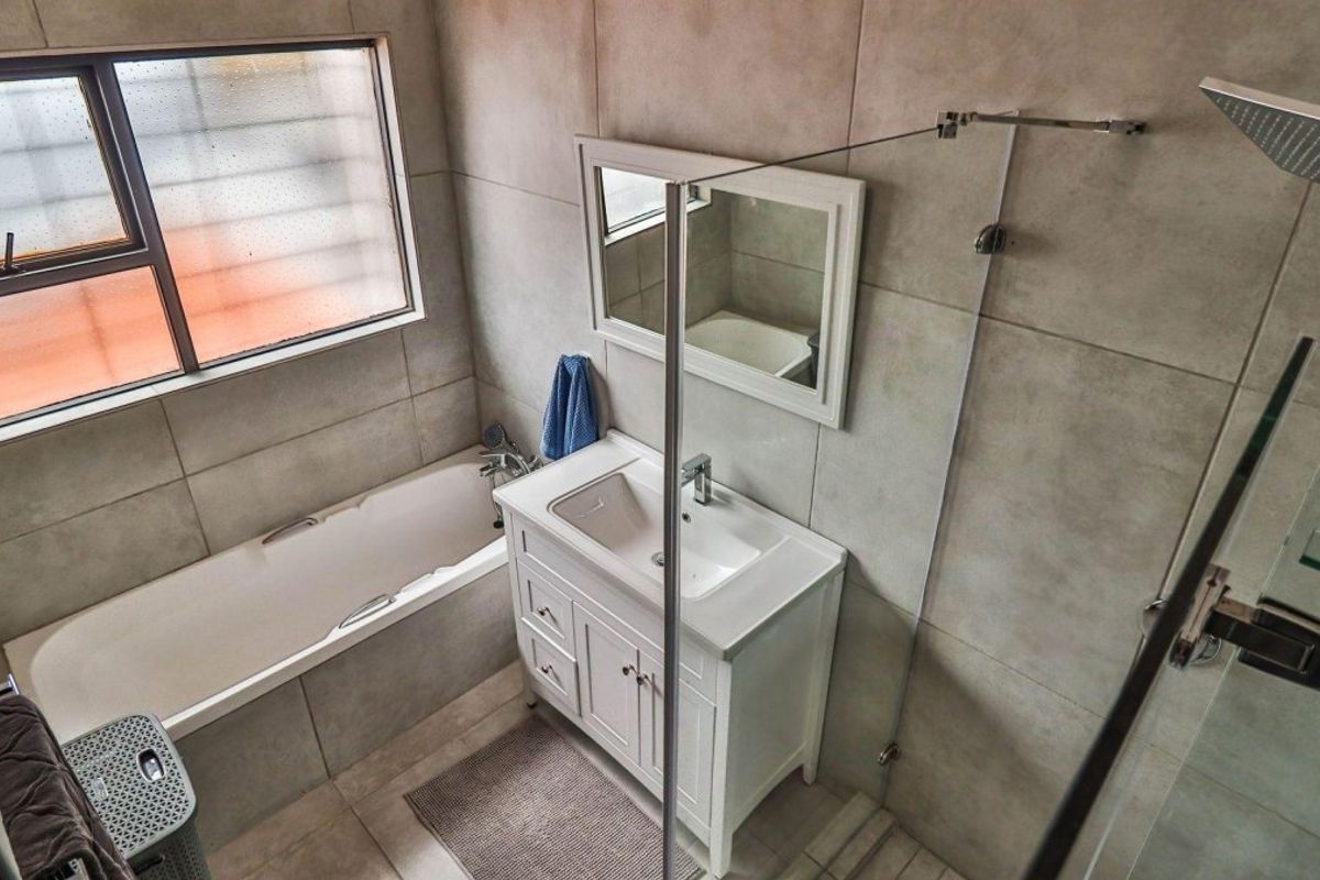 Modern bathroom featuring a bathtub, separate glass-enclosed shower, vanity basin with storage, and neutral wall tiling.