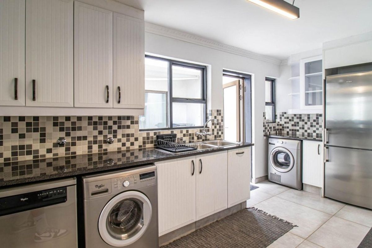 A functional kitchen featuring granite countertops, mosaic tile backsplash, ample built-in cabinetry, and integrated space for laundry appliances.