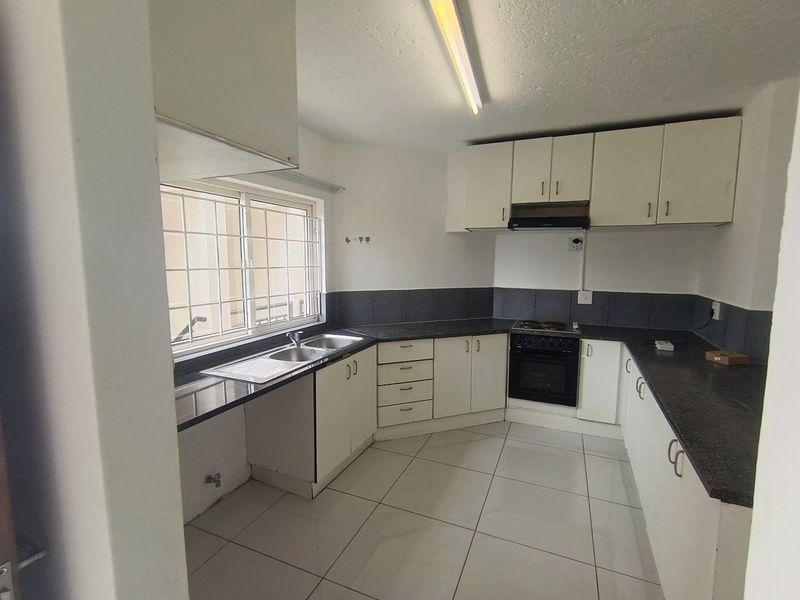 A functional kitchen featuring white cabinetry, dark countertops, tiled flooring, and built-in cooking appliances, offering a clean and practical workspace.