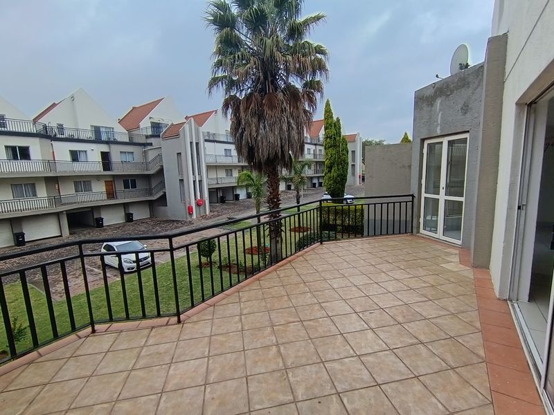 A spacious tiled balcony with metal railings, overlooking the townhouse complex courtyard and communal garden area.