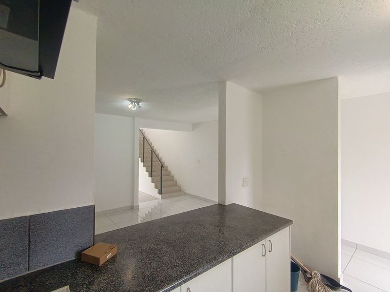 Open plan kitchen area featuring granite countertops and built-in cabinetry, leading to a staircase with a metal railing in a bright, tiled interior space.