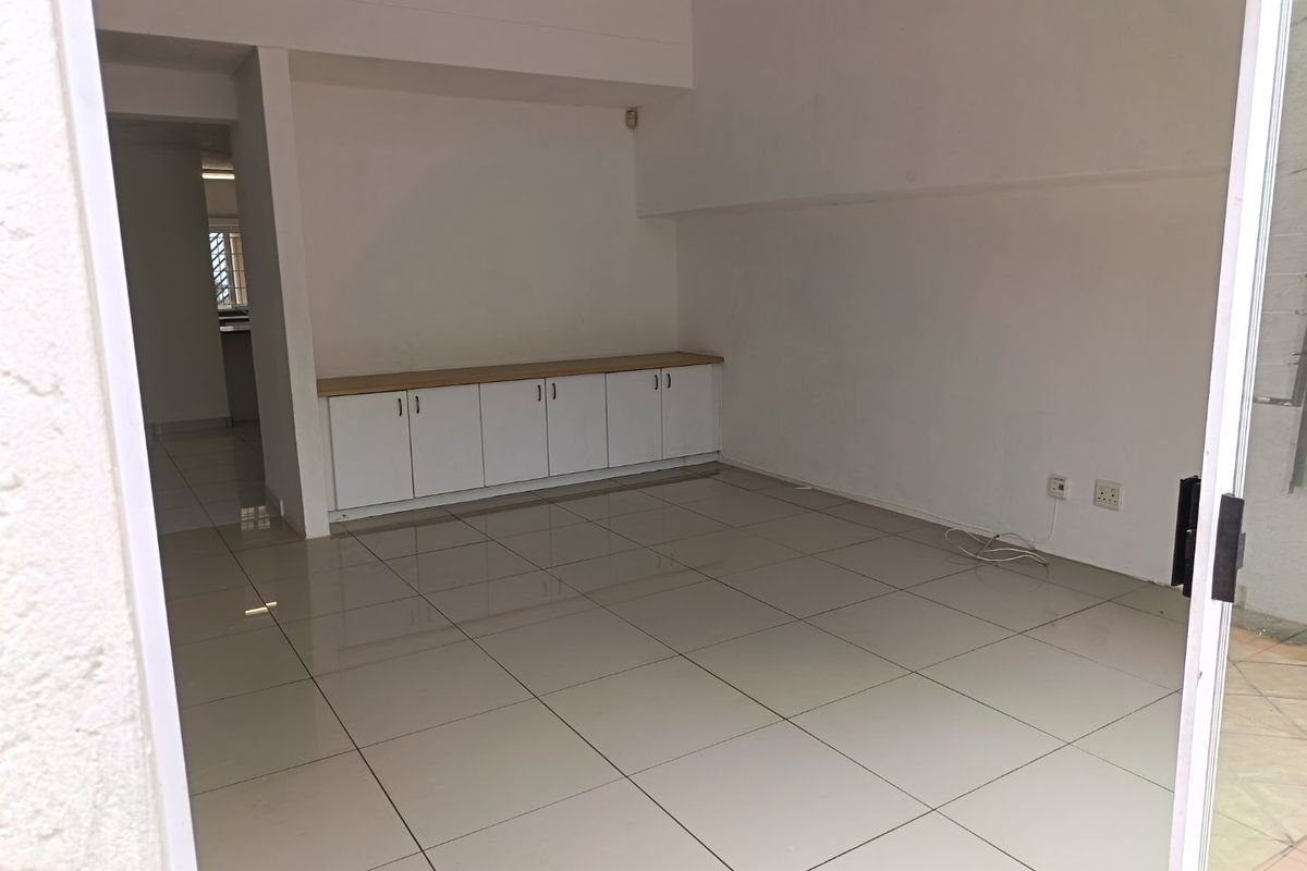 An empty, open-plan living area featuring neutral tiled flooring and built-in low-level cabinetry, offering a clean and versatile space.
