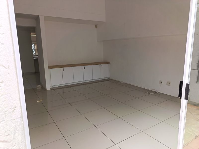An empty, open-plan living area featuring neutral tiled flooring and built-in low-level cabinetry, offering a clean and versatile space.