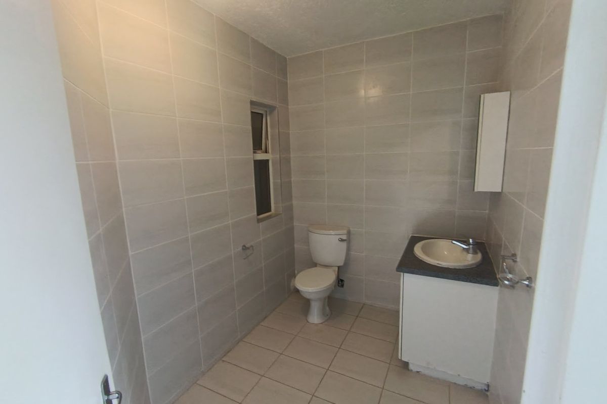 A functional bathroom featuring full-height wall tiling, a floor-mounted toilet, and a vanity unit with a basin.