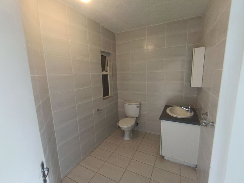 A functional bathroom featuring full-height wall tiling, a floor-mounted toilet, and a vanity unit with a basin.