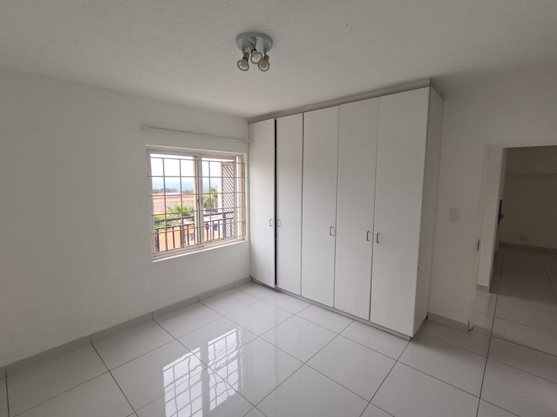 A bright, empty bedroom featuring white built-in cupboards, tiled flooring, and a window with security bars.