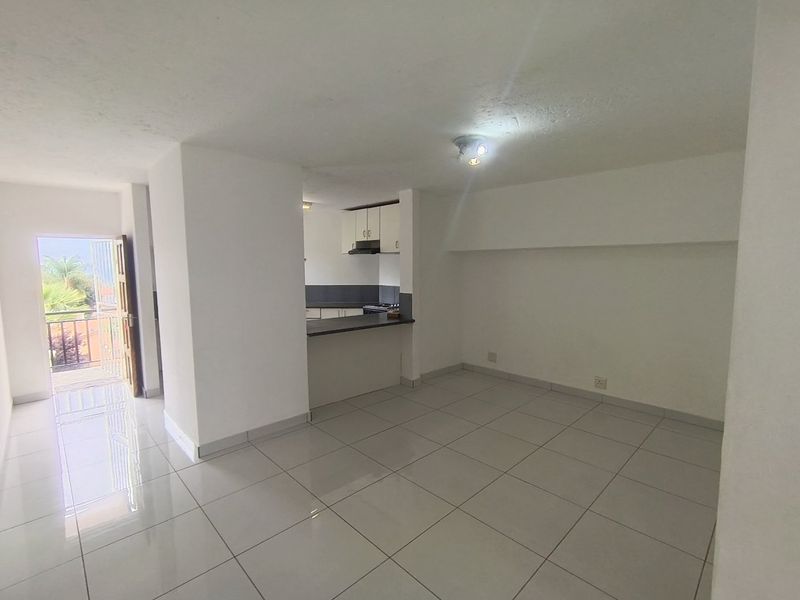An open-plan living and kitchen area featuring neutral tiled flooring, a breakfast bar, and direct access to a balcony.