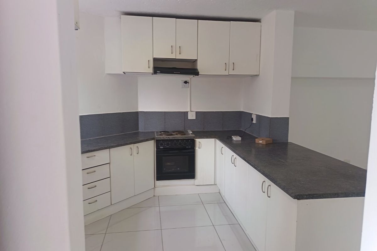 A functional kitchen featuring white cabinetry, dark laminate countertops, tiled flooring, and a built-in electric oven and hob.