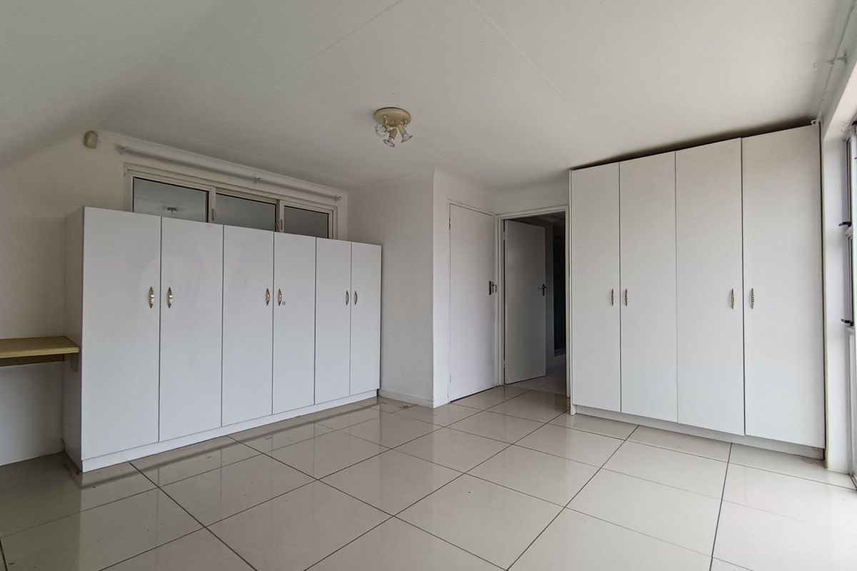 A spacious, empty bedroom featuring neutral tiled flooring and extensive built-in white cabinetry for ample storage.