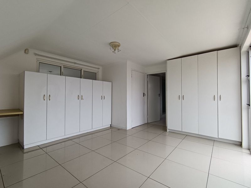A spacious, empty bedroom featuring neutral tiled flooring and extensive built-in white cabinetry for ample storage.