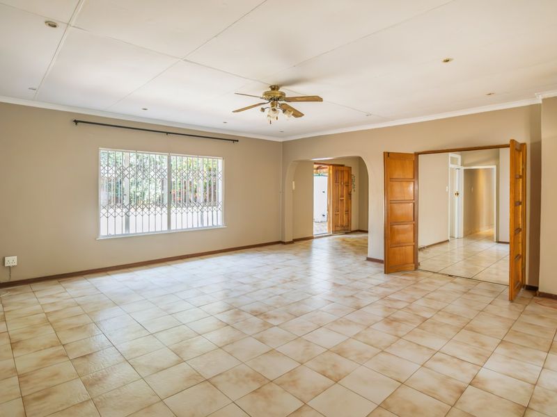 Spacious, empty living area featuring neutral walls, tiled flooring, a ceiling fan, and an arched entryway leading to the rest of the home.