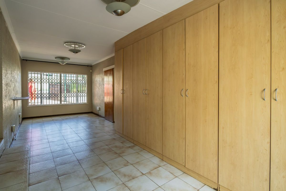 Spacious bedroom featuring extensive built-in cupboards, tiled flooring, and a security gate on the window, offering a clean and functional living space.