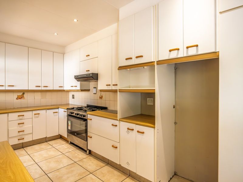 A functional kitchen featuring white cabinetry, laminate countertops, a gas stove with extractor fan, and tiled flooring throughout.