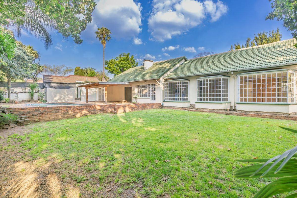 Rear view of the property featuring a spacious lawn, swimming pool, covered patio area, and classic bay windows with security bars.