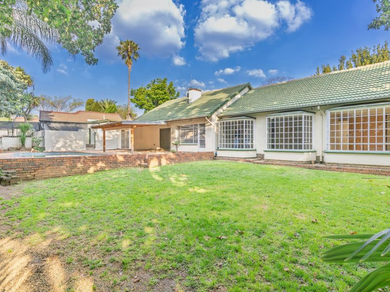 Rear view of the property featuring a spacious lawn, swimming pool, covered patio area, and classic bay windows with security bars.