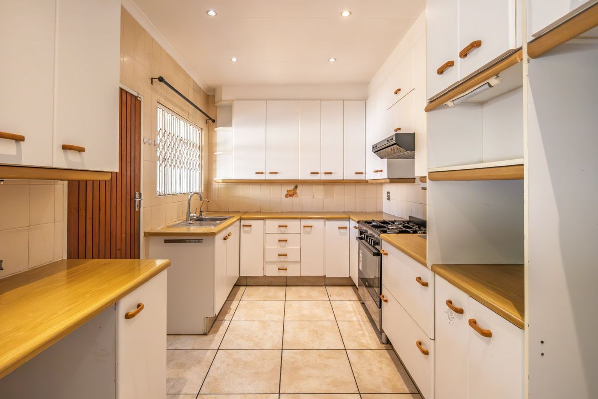 A functional kitchen featuring white built-in cabinetry, laminate countertops, a gas stove with extractor fan, and tiled flooring.