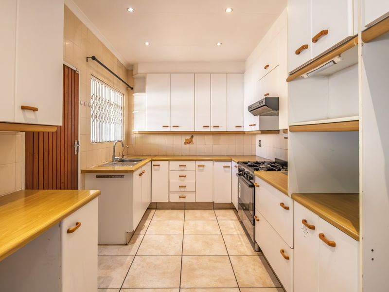 A functional kitchen featuring white built-in cabinetry, laminate countertops, a gas stove with extractor fan, and tiled flooring.