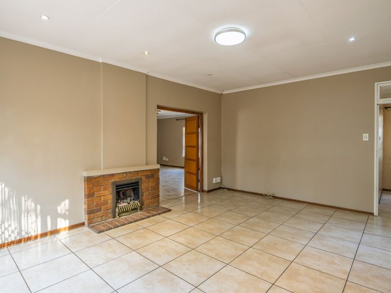Spacious living room featuring neutral walls, ceramic floor tiles, and a classic brick fireplace, offering a clean and versatile layout.