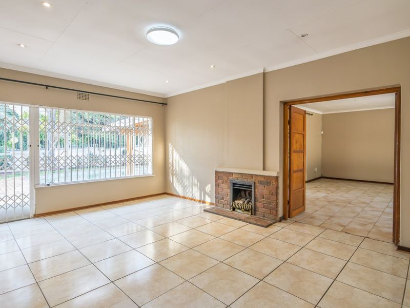 Spacious living room featuring ceramic floor tiles, a brick fireplace, and large windows with security gates, leading into an adjacent room.