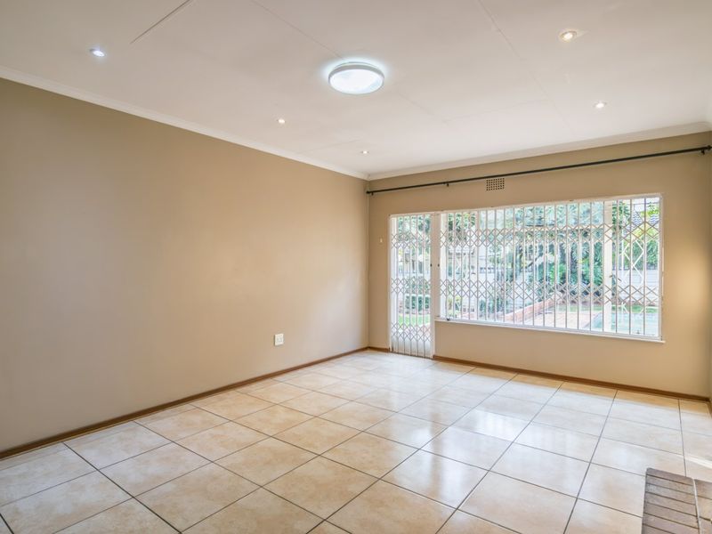 Spacious, empty living area featuring neutral tiled flooring, recessed lighting, and a secure window with metal security bars overlooking the exterior.