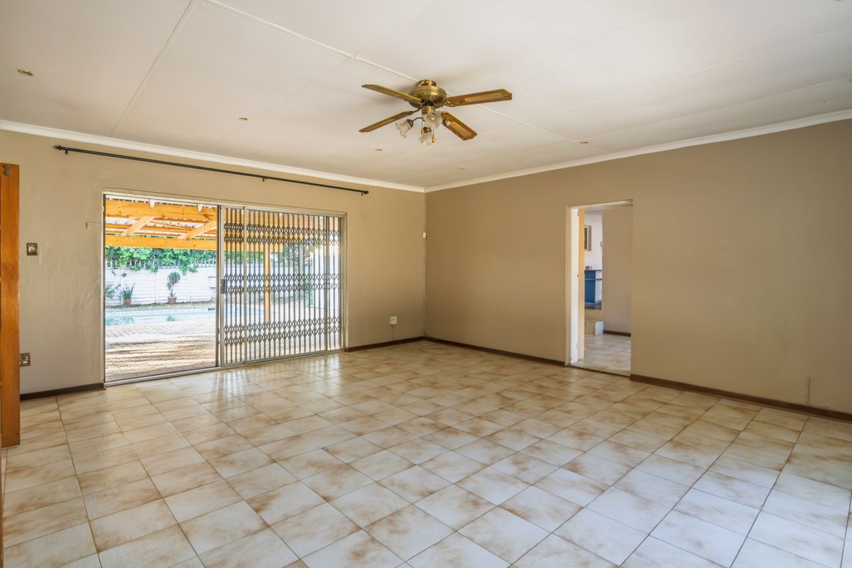 Spacious, empty living room featuring tiled flooring, a ceiling fan, and sliding glass doors providing access to the outdoor patio and pool area.