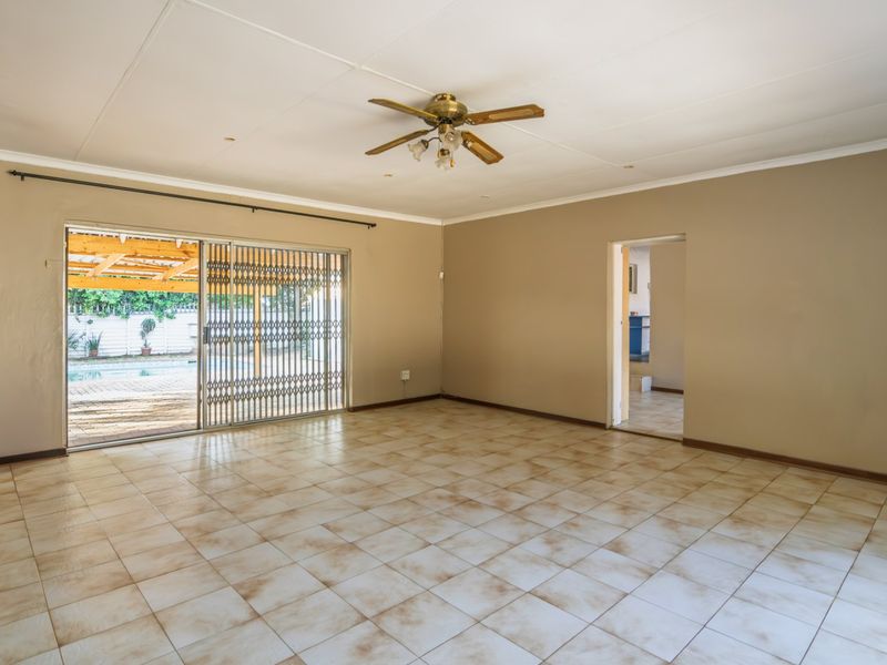 Spacious, empty living room featuring tiled flooring, a ceiling fan, and sliding glass doors providing access to the outdoor patio and pool area.