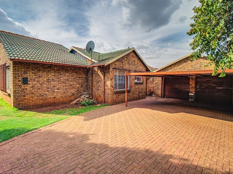 Front view of a face brick house featuring a tiled roof, paved driveway, and a covered carport area.