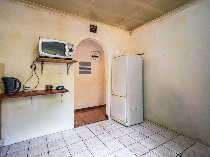 A dated kitchen area featuring tiled flooring, an arched doorway, and wall-mounted shelving, requiring cosmetic updates and refurbishment to improve its overall condition.