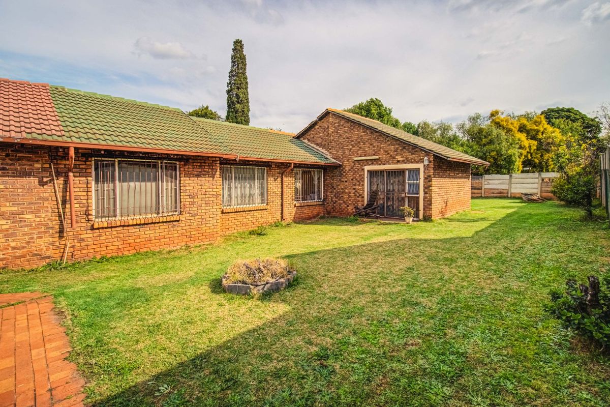 Rear view of a face-brick house featuring a tiled roof, security-barred windows, and a sliding door leading to a spacious backyard.