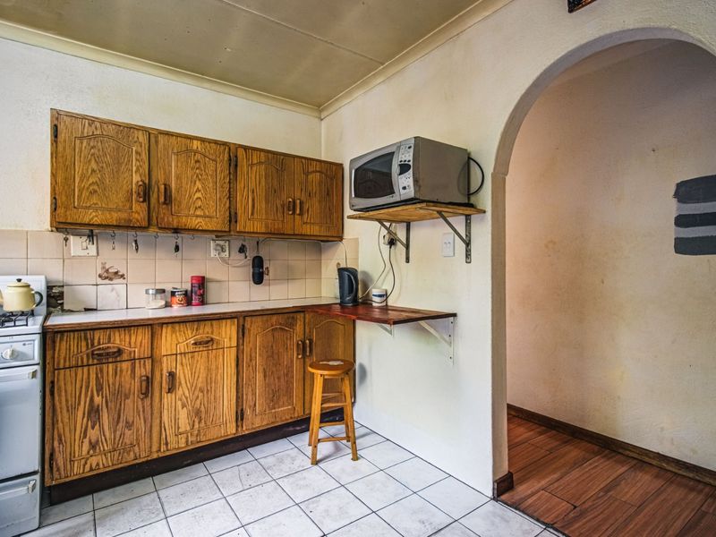 A dated kitchen featuring wooden cabinetry, tiled backsplash, and a gas stove, leading through an archway into an adjacent room with laminate flooring.