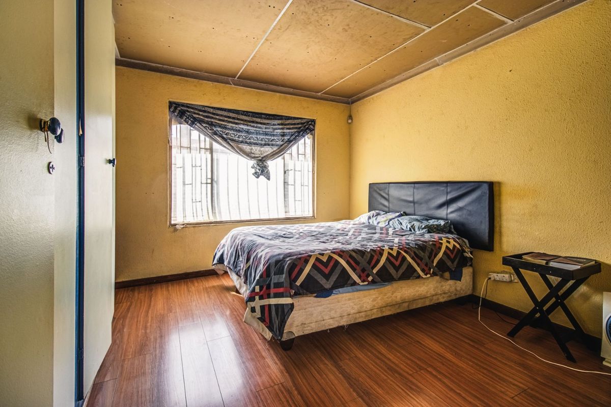 A bedroom featuring laminate flooring and security bars on the window, requiring cosmetic updates to the ceiling and wall finishes.