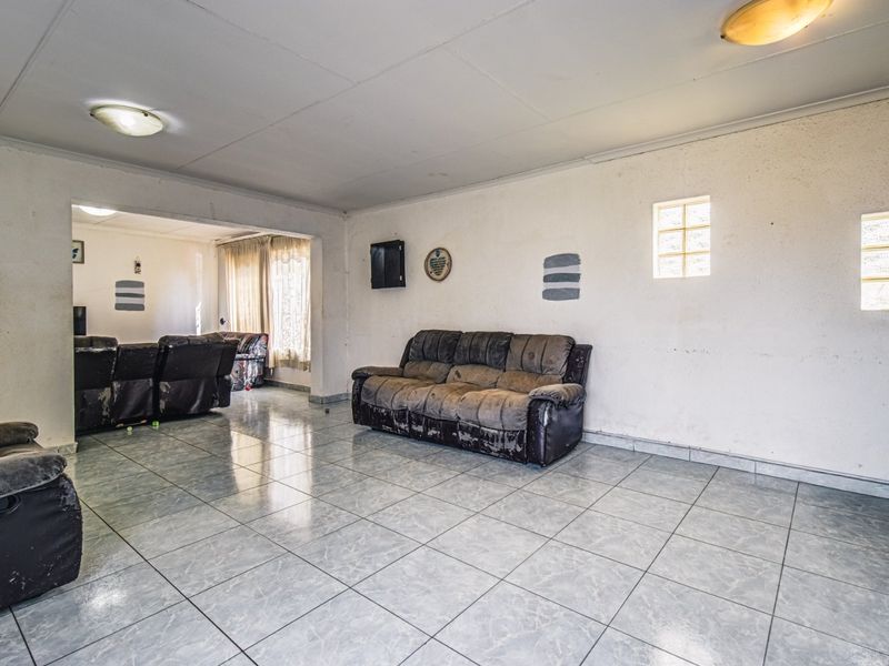 Spacious open-plan living area featuring tiled flooring, glass block windows, and neutral wall finishes, offering a versatile layout for modern living.