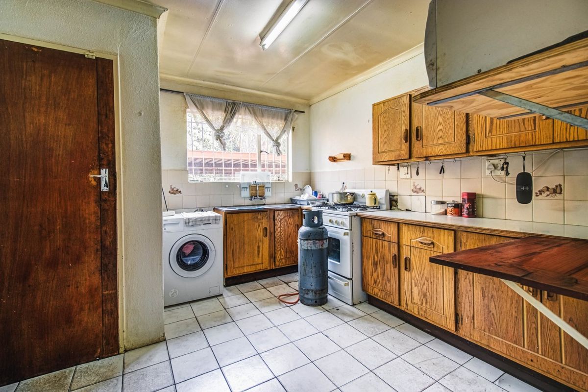 A dated kitchen featuring wooden cabinetry, tiled flooring, and a gas stove, requiring cosmetic updates to modernize the space.