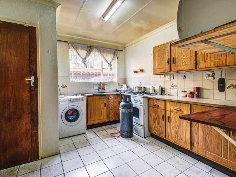A dated kitchen featuring wooden cabinetry, tiled flooring, and a gas stove, requiring cosmetic updates to modernize the space.
