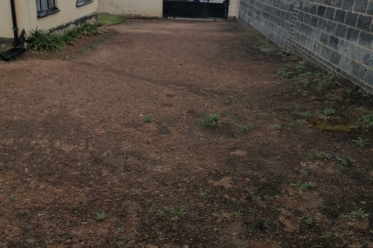 A spacious rear yard area featuring a concrete block boundary wall, metal gate, and electric fencing, currently awaiting landscaping and ground cover.