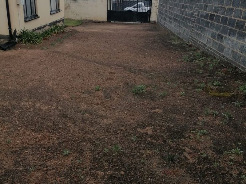 A spacious rear yard area featuring a concrete block boundary wall, metal gate, and electric fencing, currently awaiting landscaping and ground cover.