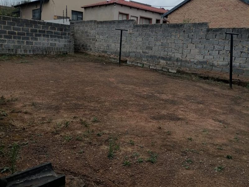 A spacious, unlandscaped rear yard enclosed by concrete block boundary walls, featuring metal washing line poles and a concrete drainage channel.