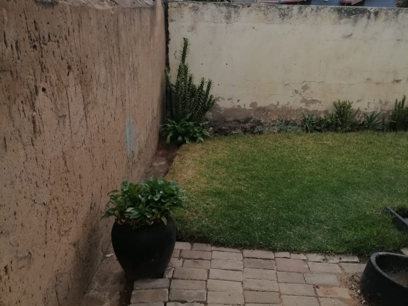 A rear garden area featuring a small lawn, paved patio section, and high boundary walls requiring maintenance and repair.