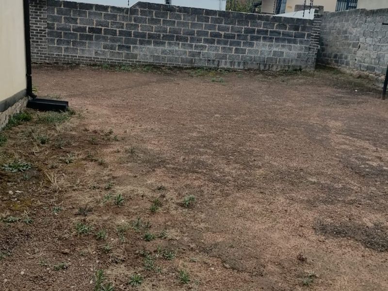 A spacious rear yard area featuring a perimeter boundary wall with electric fencing, offering a blank canvas for landscaping and outdoor development.