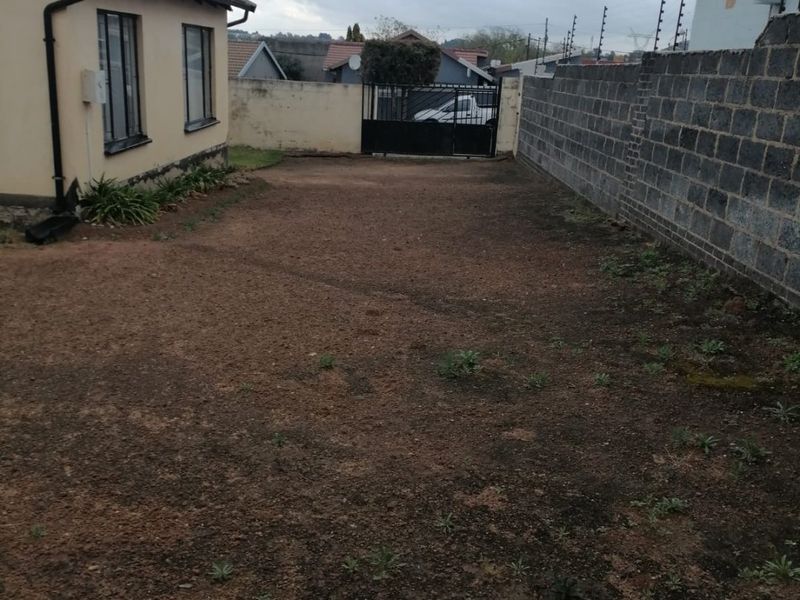 A rear yard area featuring a perimeter wall, metal gate, and electric fencing, with an unlandscaped ground surface.