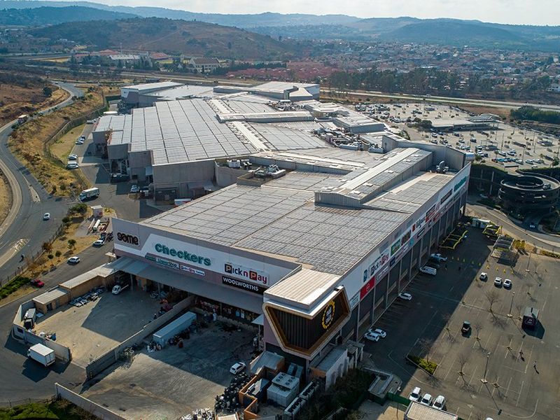 Aerial view of a large commercial shopping center featuring extensive rooftop solar panels, dedicated loading bays, and ample surface and multi-level parking facilities.