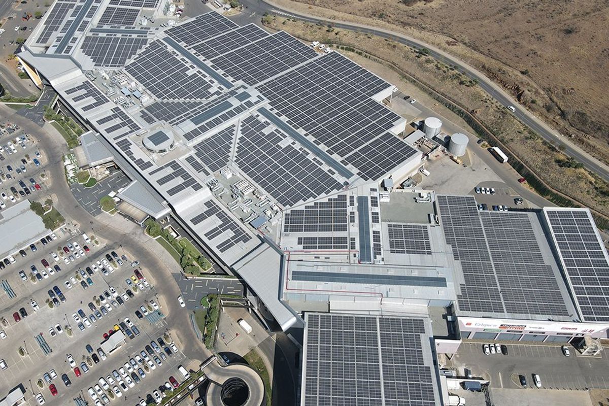 Aerial view of a large commercial shopping center featuring extensive rooftop solar panel installations, HVAC infrastructure, and surrounding asphalt parking facilities.