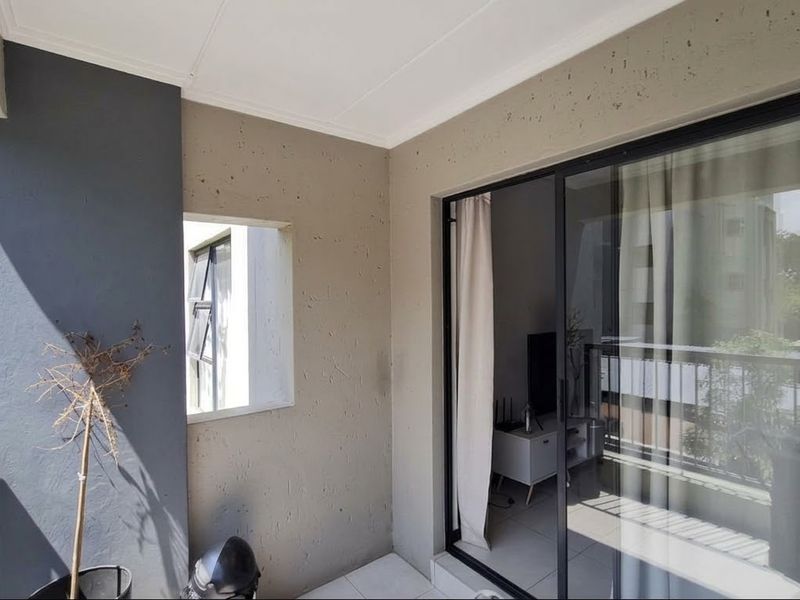 A private balcony featuring tiled flooring, textured walls, and a sliding glass door providing access to the interior living space.