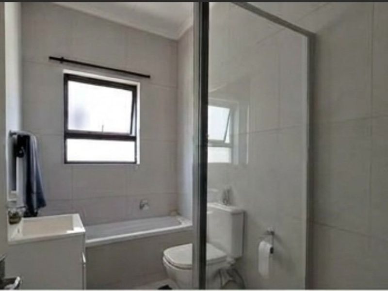 A functional bathroom featuring a bathtub, toilet, vanity, and a glass shower screen with neutral wall tiling.