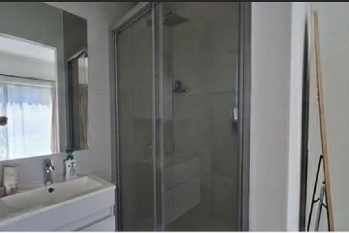 A modern bathroom featuring a vanity with basin, wall-mounted mirror, and a glass-enclosed shower unit with fixed shower head.