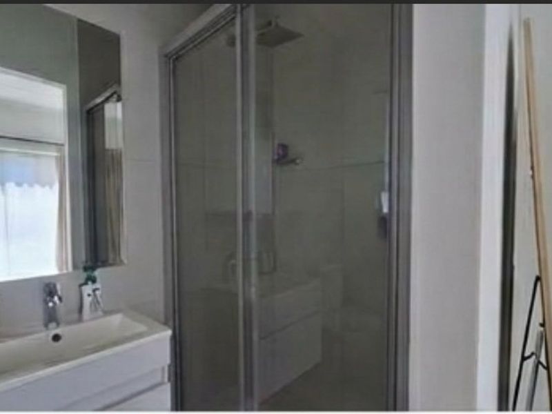 A modern bathroom featuring a vanity with basin, wall-mounted mirror, and a glass-enclosed shower unit with fixed shower head.