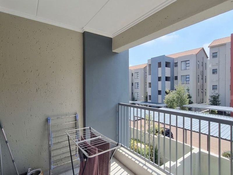 A covered balcony featuring a metal balustrade and textured wall finishes, offering an open view of the surrounding apartment complex.