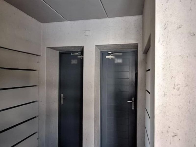 A clean, modern apartment hallway featuring two secure entry doors with integrated door closers and textured wall finishes.